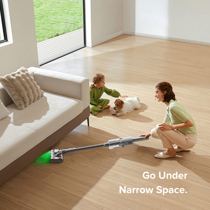 Woman using a vacuum cleaner to clean under a couch with a child and dog nearby.